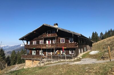 Bauernhof Adlern Zweistöckiges Holzhaus mit Balkonen am Hang vor blauem Himmel.