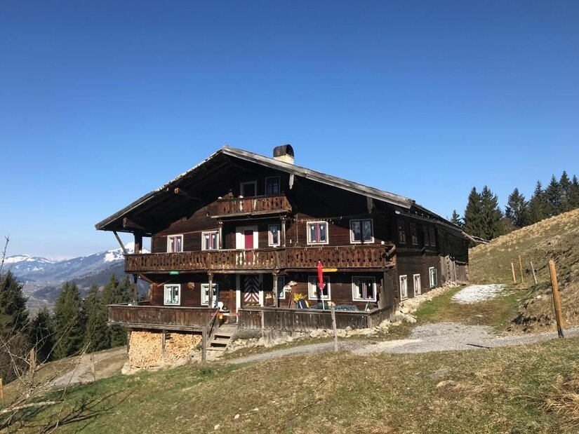 Zweistöckiges Holzhaus mit Balkonen am Hang vor blauem Himmel.