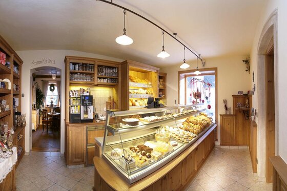 Bäckerei und Café Krumma Reith Innenansicht einer Bäckerei mit Glastheke voller Kuchen und Gebäck sowie Holzregalen im Hintergrund.