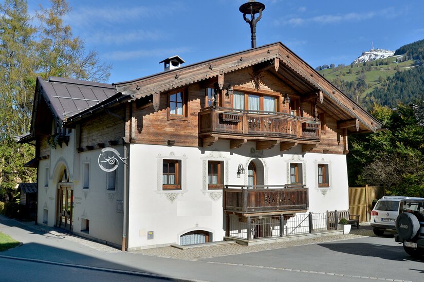 Ploderhaus Appartement Wilder Kaiser Alpines Wohnhaus mit weißer Fassade, Holzbalkonen und Satteldach vor bewaldeten Bergen.