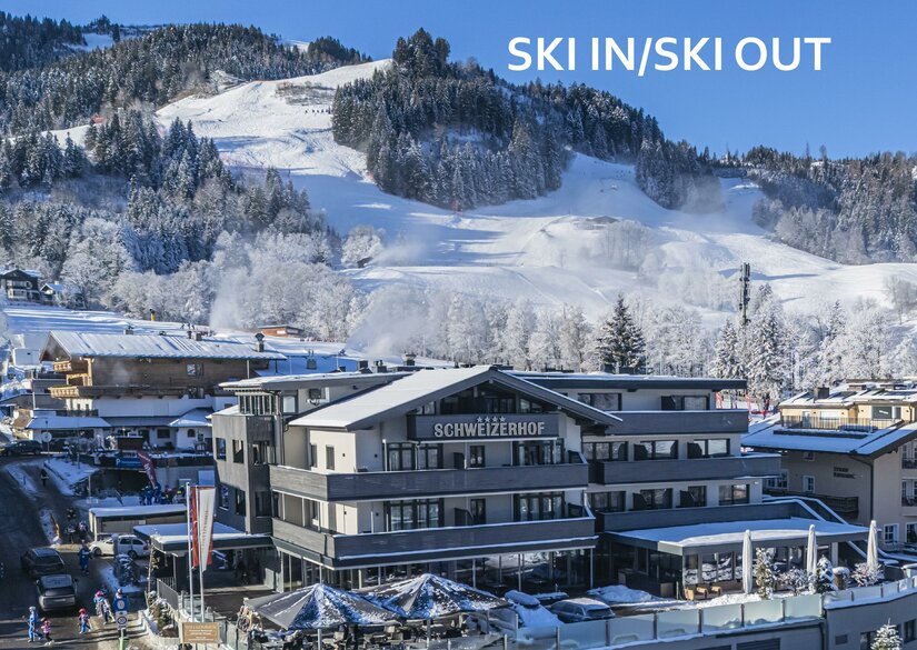 Hausansicht SKI IN SKI OUT <p>Das moderne Hotel Schweizerhof mit Restaurant in einer verschneiten Berglandschaft. Im Hintergrund ist die Streifabfahrt des Hahnenkamms sichtbar.</p>