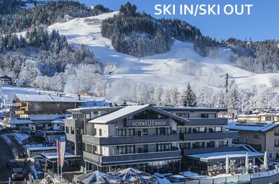Hausansicht SKI IN SKI OUT <p>Das moderne Hotel Schweizerhof mit Restaurant in einer verschneiten Berglandschaft. Im Hintergrund ist die Streifabfahrt des Hahnenkamms sichtbar.</p>