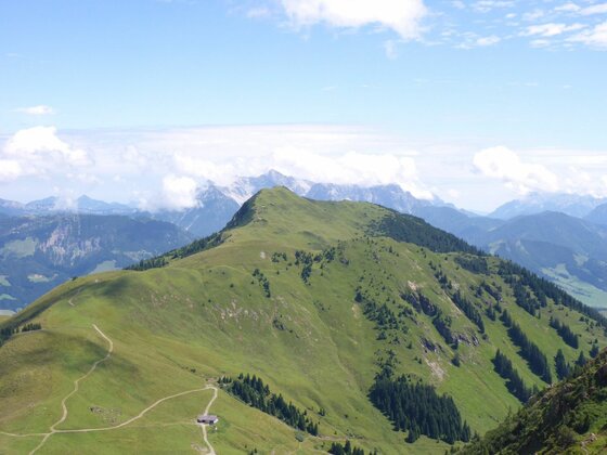 Gipfelpanorama am Stuckkogel Blick auf den grünen Bergrücken des Stuckkogels mit Wanderwegen und einer kleinen Hütte unter blauem Himmel.