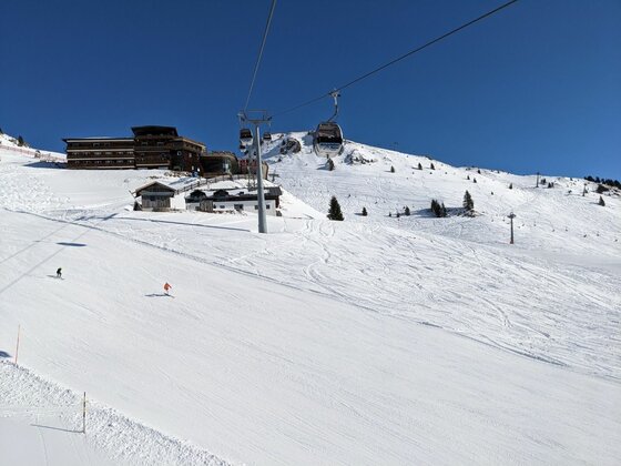 Blick auf eine Skipiste mit Gondelbahn und Bergstation vor blauem Himmel.