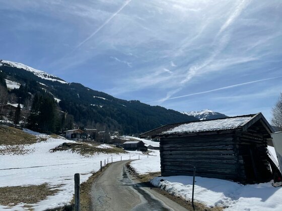 Weg bei der Schwimmbadrunde Verschneite Berglandschaft mit einem asphaltierten Weg und einer Holzhütte im Vordergrund.
