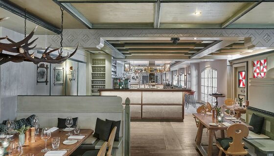 Neuwirt Barblick Innenansicht eines Restaurants mit Holztischen, einer zentralen Bar und dekorativem Hirschgeweih an der Decke.