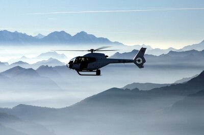 Ein Hubschrauber schwebt über einer beeindruckenden Berglandschaft. Der Himmel ist klar und die Berge sind von Nebel umgeben.