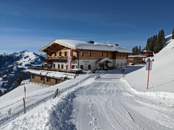 Schneebedeckte Bichlalm in den Alpen mit präpariertem Winterwanderweg im Vordergrund.