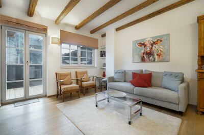 Wohnzimmer mit grauem Sofa, zwei Sesseln, Holzbalkendecke und einem Kuhgemälde an der Wand.