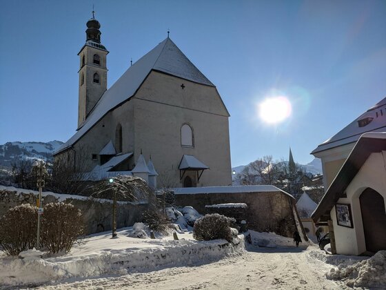 Kirche im Winter Weiße Kirche mit Glockenturm in verschneiter Berglandschaft bei Sonnenschein.