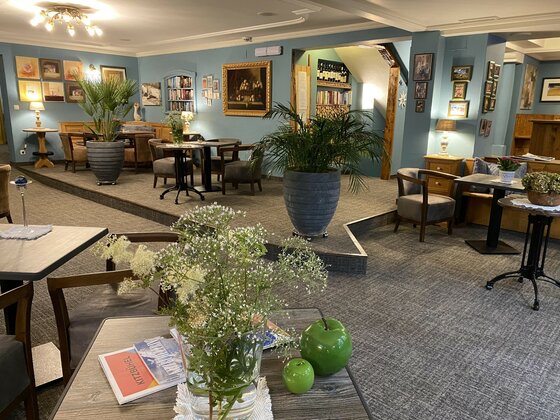 Loungebereich eines Hotels mit blauen Wänden, Sitzgruppen, Zimmerpflanzen und Bildern.