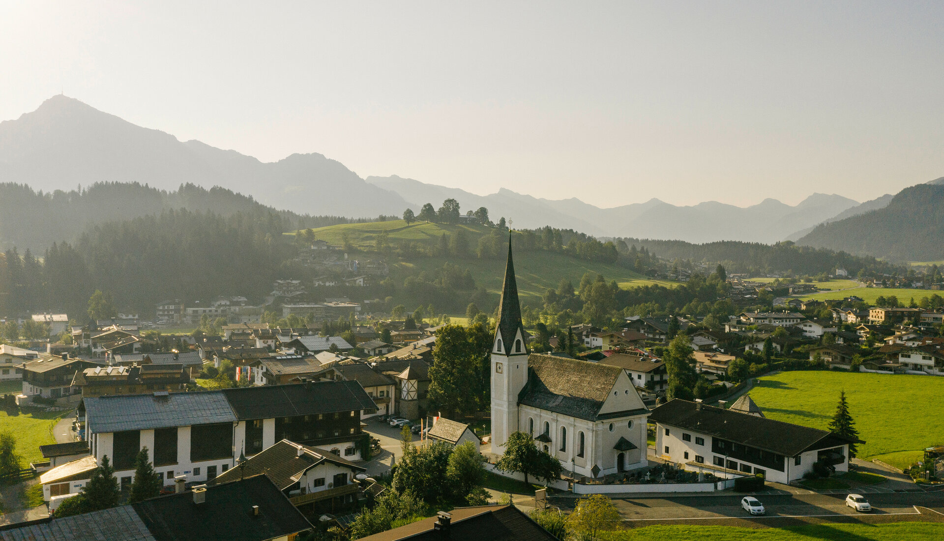 Reith bei Kitzbühel mit Kirche und Hügeln, umgeben von Bergen.
