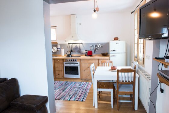 Kitzbühel Retro Apartment Küche Esstisch Küche mit Holzfronten, weißem Esstisch, Retro-Kühlschrank und TV-Gerät an der Wand.
