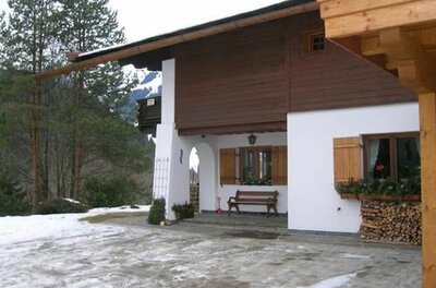 Außenansicht Haus Filzer im Winter Alpines Wohnhaus mit weißer Fassade, Holzverkleidung und einer Bank vor dem Eingang im Schnee.