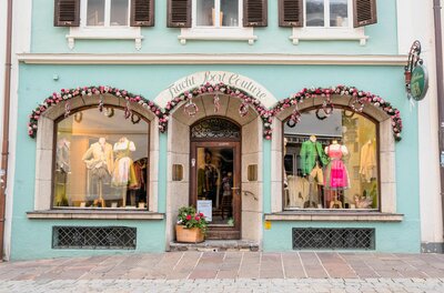 Fassade eines Trachtengeschäfts mit Schaufenstern, die Dirndl und Lederhosen auf Puppen zeigen.