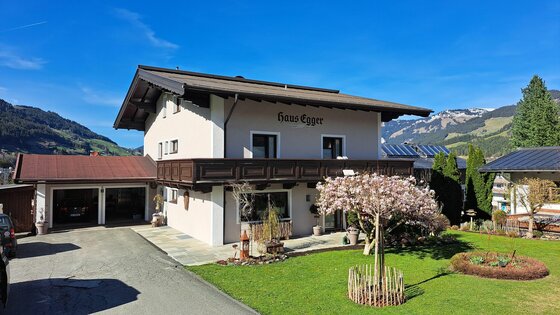 Haus Egger Außenansicht Zweistöckiges Wohnhaus mit Holzbalkon, Garten und Garage vor Bergkulisse.
