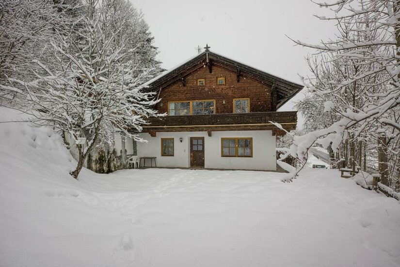 Zweistöckiges Holzhaus mit weißem Erdgeschoss in einer verschneiten Winterlandschaft.