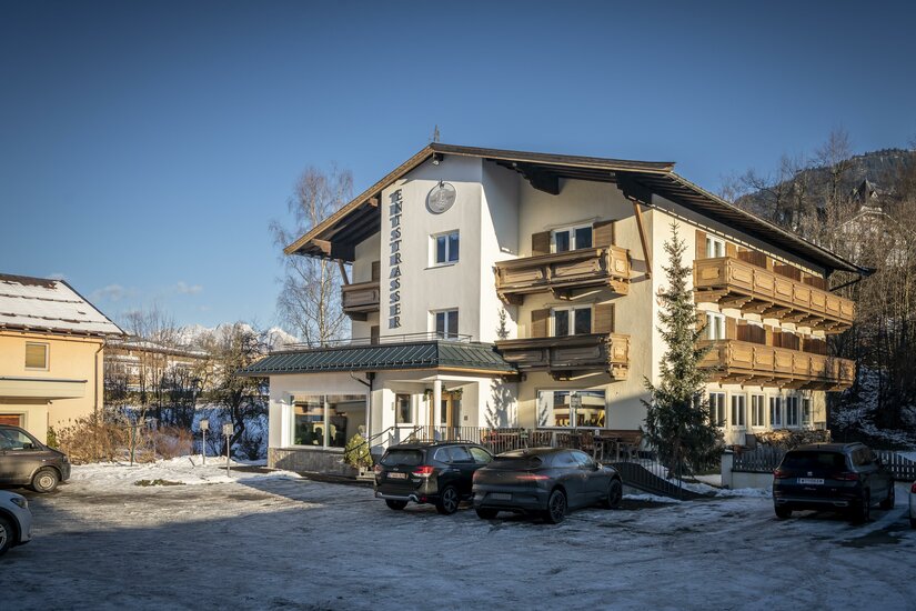 Hotel Garni Entstrasser Außenansicht Mehrstöckiges Hotelgebäude mit Holzbalkonen und Parkplatz im Winter.