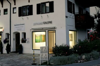 Galerie Zeitkunst Ein Gebäude mit der Aufschrift „Galerie“ auf der Vorderseite. Es befindet sich in einer malerischen Umgebung mit Blumen und einem klaren Himmel.