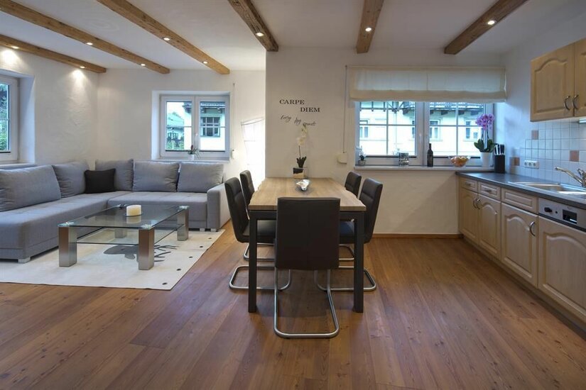 Wohnbereich Appartment Resch Moderner Wohn- und Essbereich mit grauem Ecksofa, Holztisch und Küchenzeile in einer Ferienwohnung.