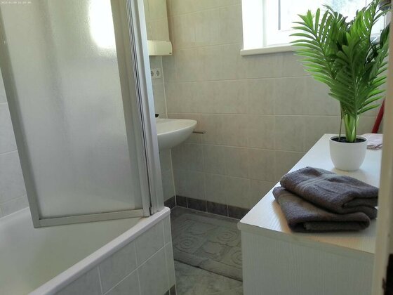 2916899_960h Ein helles Badezimmer mit einer Dusche, einem Waschbecken und einem kleinen Pflanze. Auf der Ablage liegen graue Handtücher und eine weiße Vase.