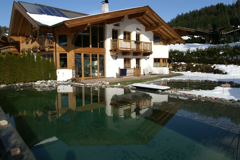 Alpines Holzhaus mit Solaranlage und Schwimmteich im Winter.