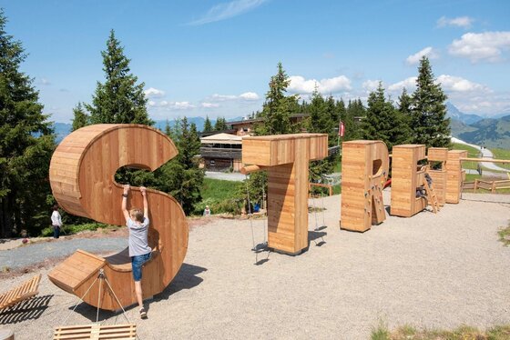 Große Holzbuchstaben als Kletterelemente auf einem Spielplatz in den Bergen.