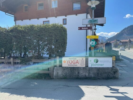 Wegweiser an der Rettenberg Runde Wegweiser für Wanderer und Radfahrer vor einem Gebäude mit Hinweisschildern für Yoga und eine Praxis.