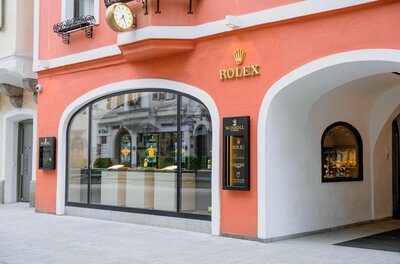 Außenansicht des Juweliergeschäfts Schroll in Kitzbühel mit lachsfarbener Fassade und Rolex-Logo.