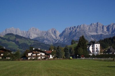 Haus Zierl vor Kaisergebirge Blick über eine grüne Wiese auf das Haus Zierl und ein weißes Schloss vor dem Gebirgsmassiv Wilder Kaiser.