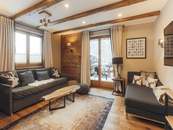 Wohnzimmer Appartement Streifblick Wohnzimmer mit zwei grauen Sofas, Holztisch, Deckenbalken und Balkontür mit Blick auf verschneite Berge.