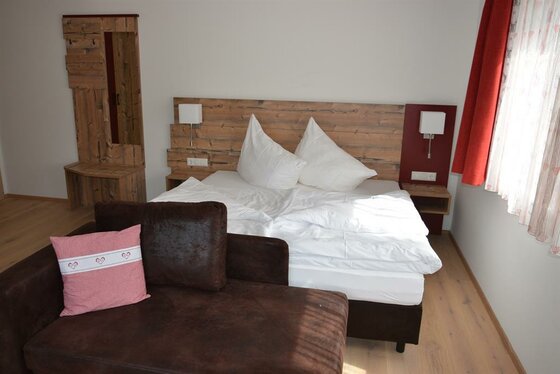 Doppelbett mit Holz-Kopfteil und braunes Sofa im Vordergrund.