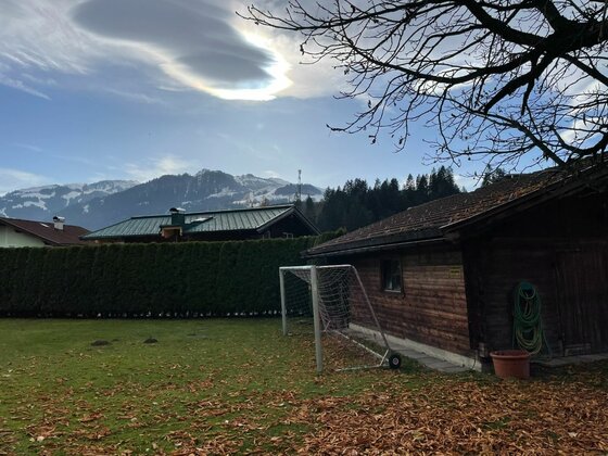 Garten mit Fußballtor und Holzhütte vor schneebedeckten Bergen unter bewölktem Himmel.
