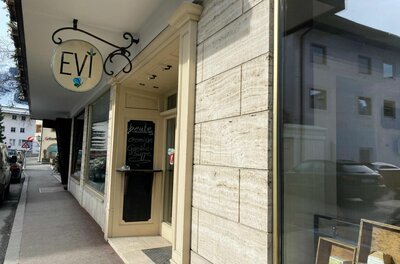 Außenansicht des Cafés Evi mit einem runden Ladenschild und einer Menütafel an der hellen Fassade.