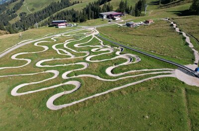 Luftaufnahme eines Mountainbike-Übungsgeländes mit vielen Kurven auf einer grünen Bergwiese.