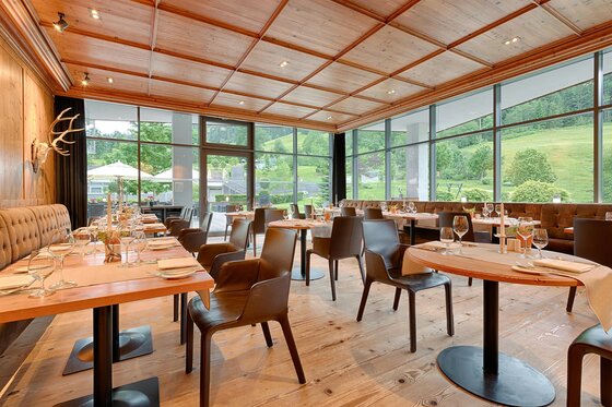 Tiroler Stube im Restaurant Steinberg Moderner Restaurantraum mit Holztischen, Lederstühlen und großen Glasfronten mit Blick ins Grüne.