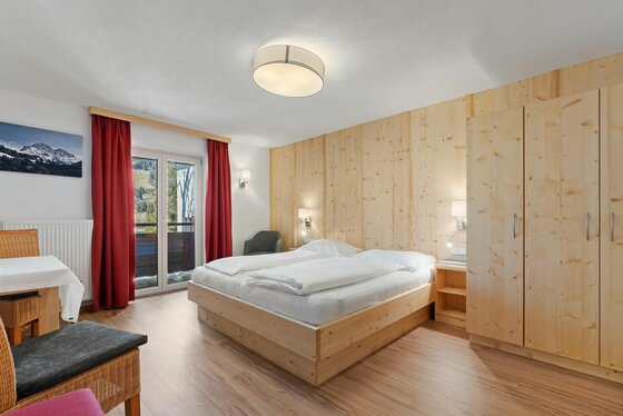 Doppelzimmer im Landhotel Jodlbühel Modernes Doppelzimmer mit hellem Holz, Balkonzugang und roten Vorhängen.