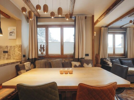 App Streifblick - Essbereich Moderner Essbereich mit Holztisch, gepolsterten Stühlen und hängenden Holzleuchten vor einem Fenster.
