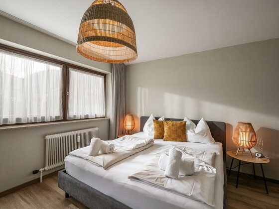 Modernes Doppelbett mit weißer Bettwäsche, gelben Kissen und Rattanlampen in einem hellen Schlafzimmer.