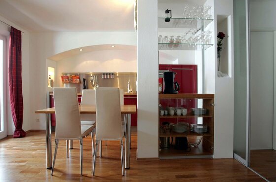 Essbereich & offene Küche Moderner Essbereich mit Holztisch und weißen Stühlen vor einer offenen Küche mit roten Fronten.
