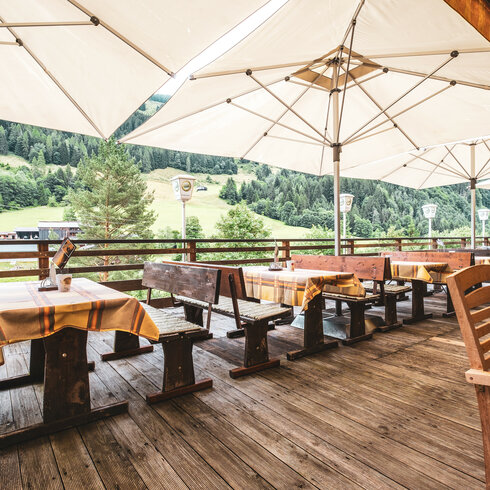 Terrasse bei der Alten Wacht in Jochberg bei Kitzbühel mit Holzmöbeln und Sonnenschirmen, umgeben von Bergen.