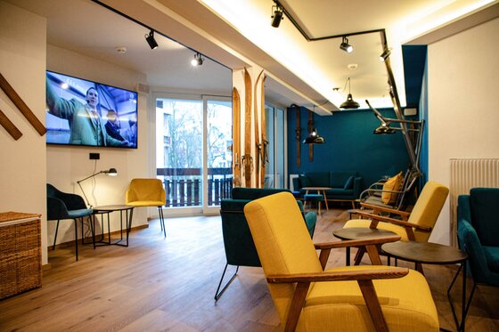 Moderner Aufenthaltsraum mit gelben und blauen Sesseln, Fernseher und dekorativen Holzskiern an der Wand.