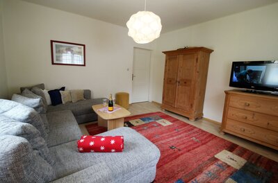 Wohnzimmer mit grauem Ecksofa, Holztisch, rotem Teppich, Schrank und Fernseher.