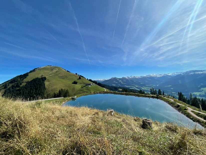 Speichersee bei Hopfgarten Ein künstlicher Speichersee auf einem Bergrücken vor grasbewachsenen Gipfeln und blauem Himmel.