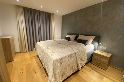 Gondelapart Schlafzimmmer Ein modernes Schlafzimmer mit einem Doppelbett und Holzfußboden. Die Wände sind in neutralen Farben gehalten, und es gibt Vorhänge sowie eine Kommode.