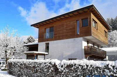 Modernes zweistöckiges Gebäude mit Holzfassade im Obergeschoss und schneebedeckter Hecke im Vordergrund.