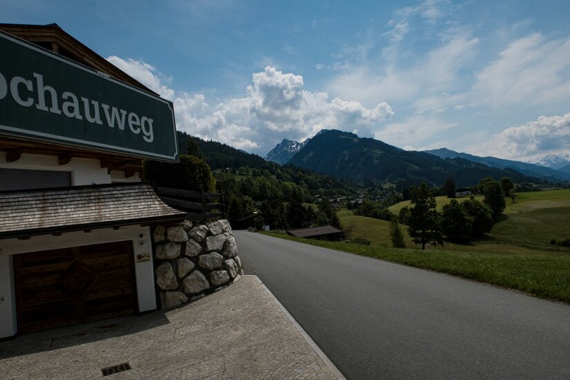 Kochauweg in Hechenmoos Asphaltierte Straße führt an einem Gebäude mit der Aufschrift Kochauweg vorbei in eine Berglandschaft.