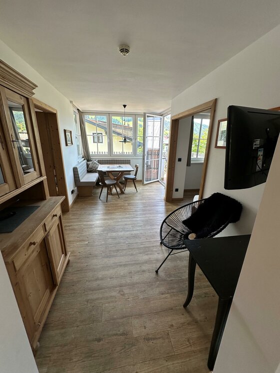 Apartment Ein heller, einladender Raum mit Holzfußboden und großen Fenstern. Es gibt einen Tisch mit Stühlen und eine moderne Fernsehecke.