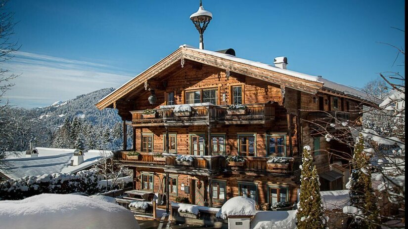 Hausansicht Winter Buccara Apartments Mehrstöckiges Holzhaus mit Balkonen und schneebedecktem Dach vor bewaldeten Bergen im Winter.