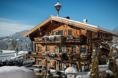 Hausansicht Winter Buccara Apartments Mehrstöckiges Holzhaus mit Balkonen und schneebedecktem Dach vor bewaldeten Bergen im Winter.